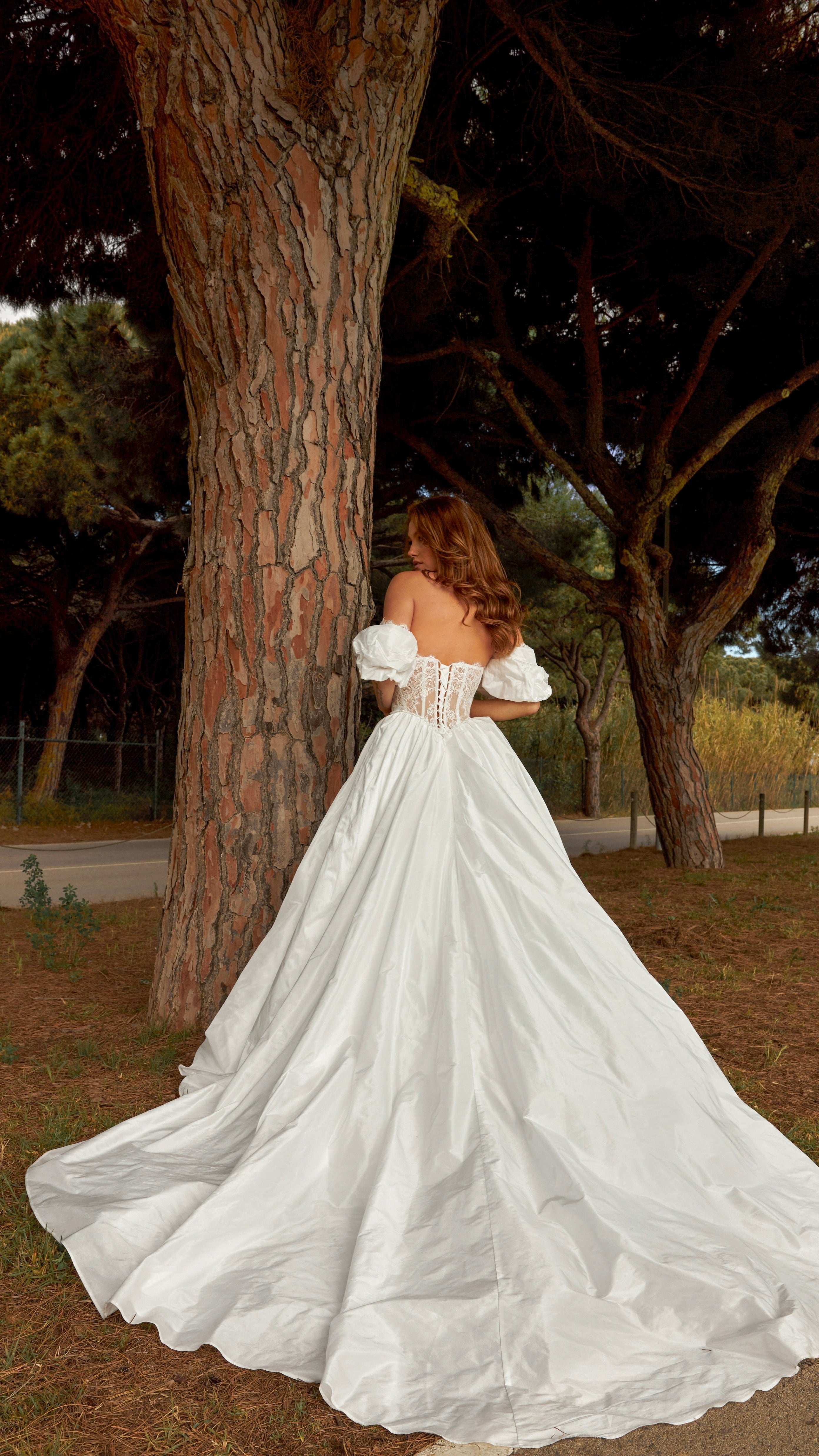Woman in a white wedding dress standing next to a tree in a natural setting