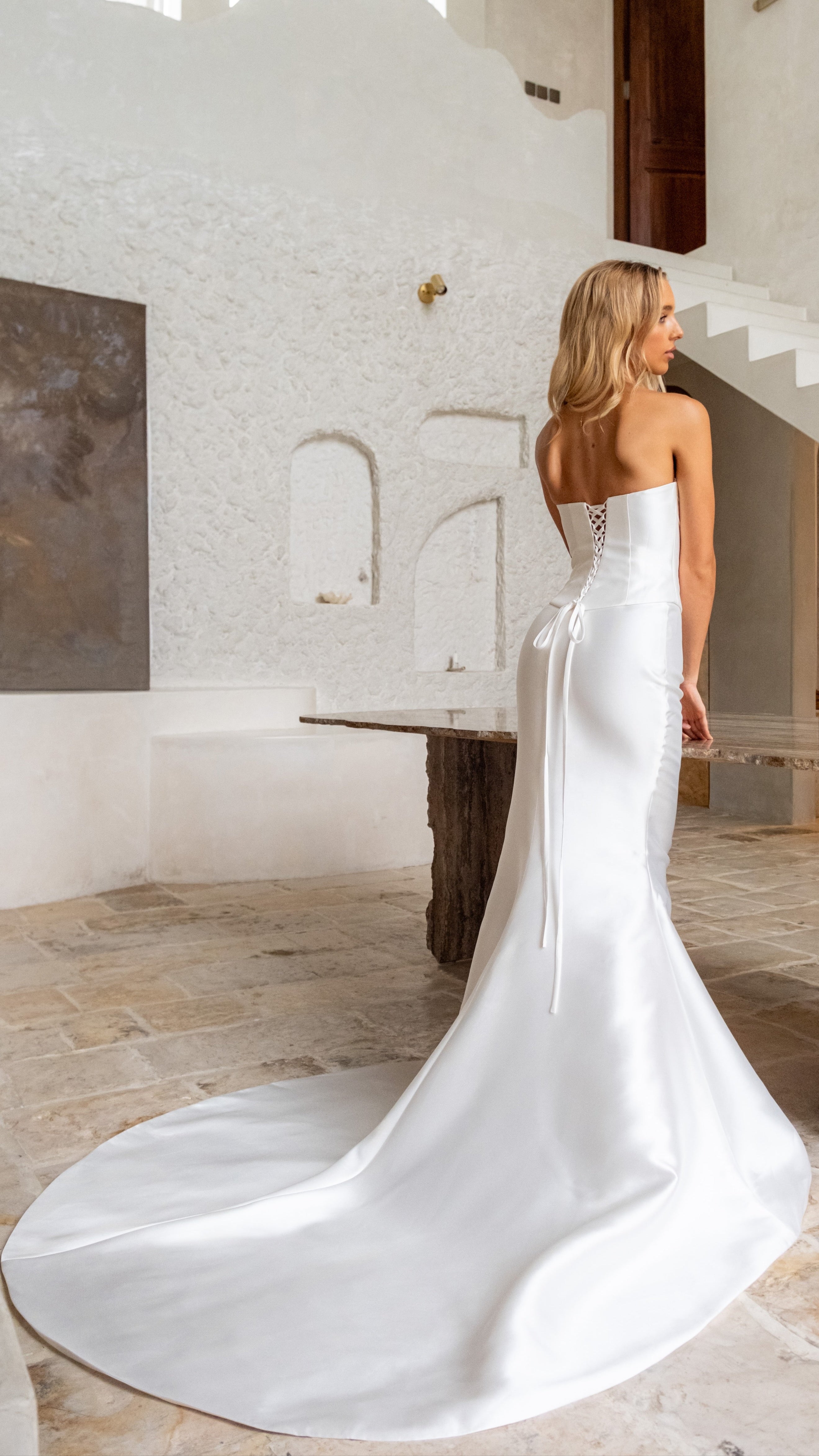 Woman in a white strapless wedding dress standing in a modern interior setting.