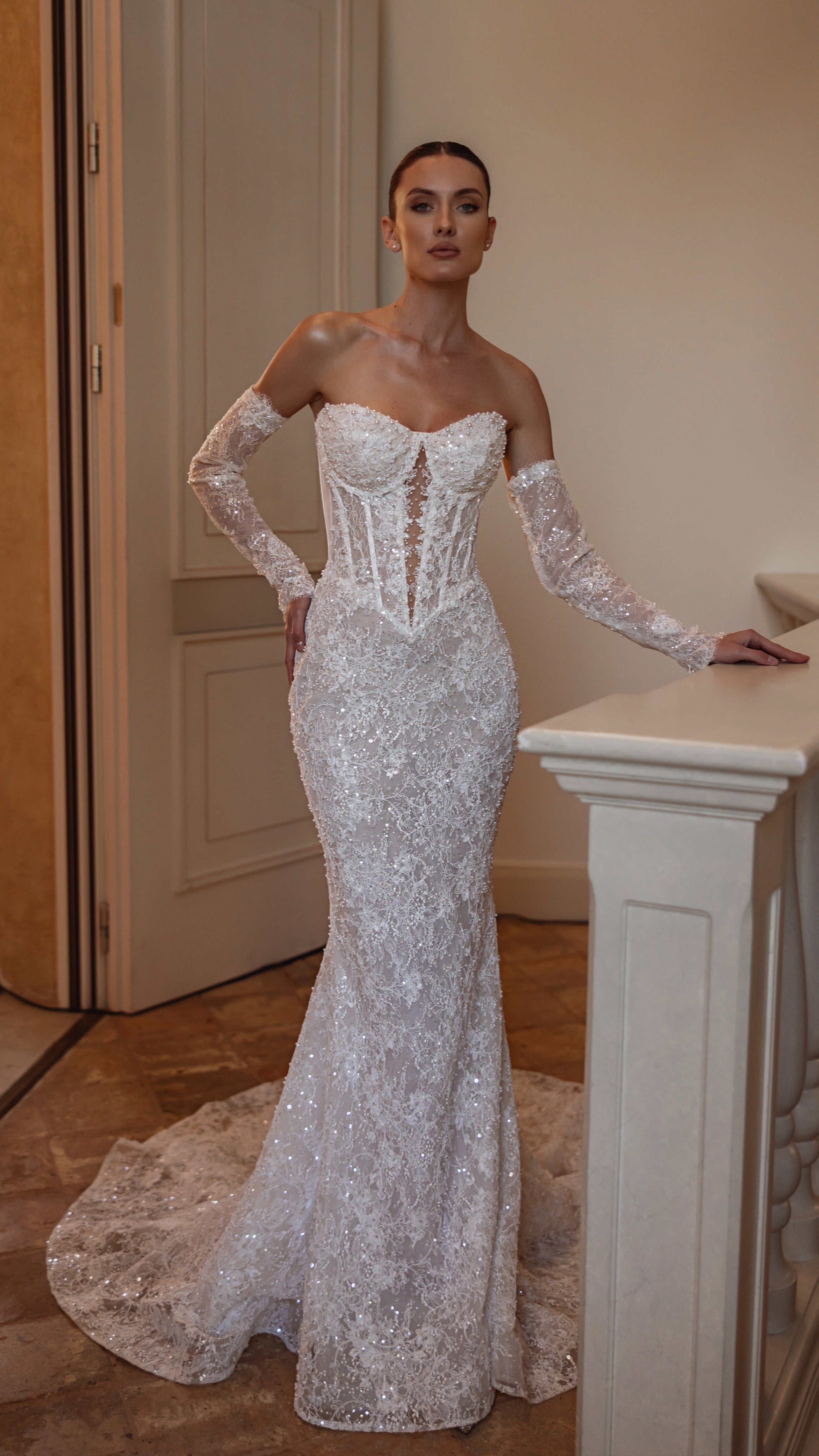 Woman in a white lace wedding dress standing indoors.