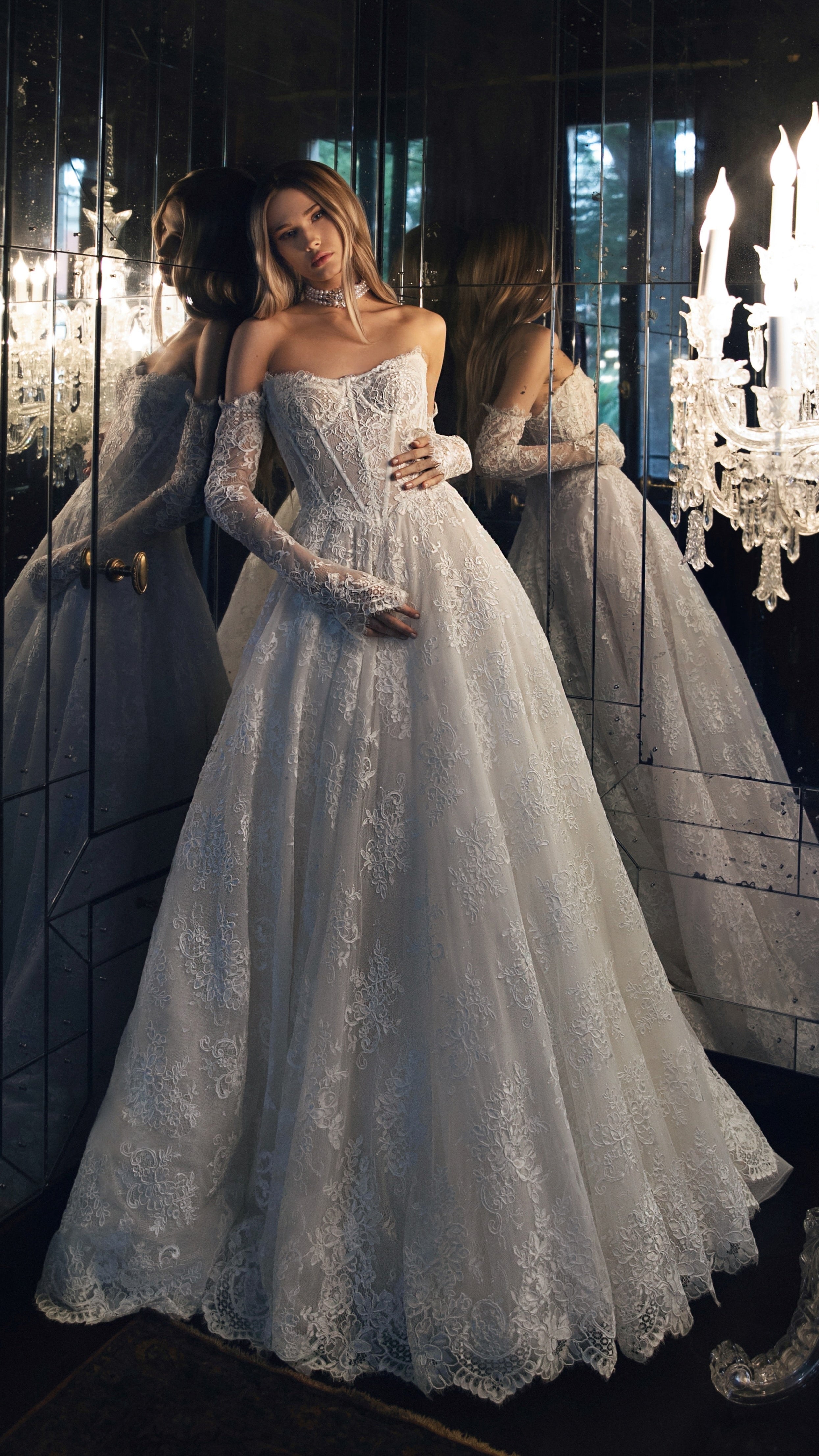 Woman in a white lace wedding dress standing in front of a chandelier.