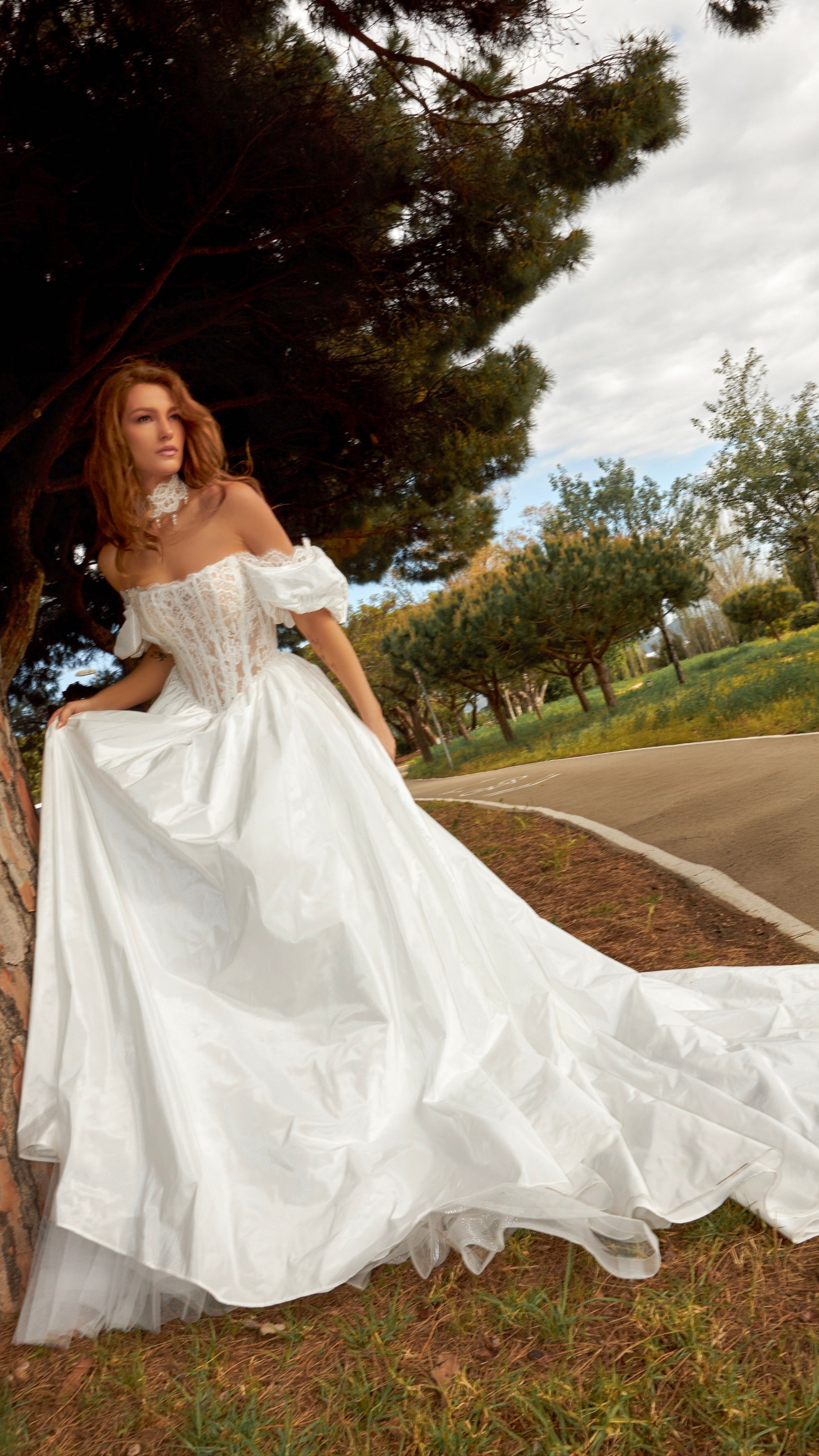 Woman in a white wedding dress standing next to a tree in an outdoor setting