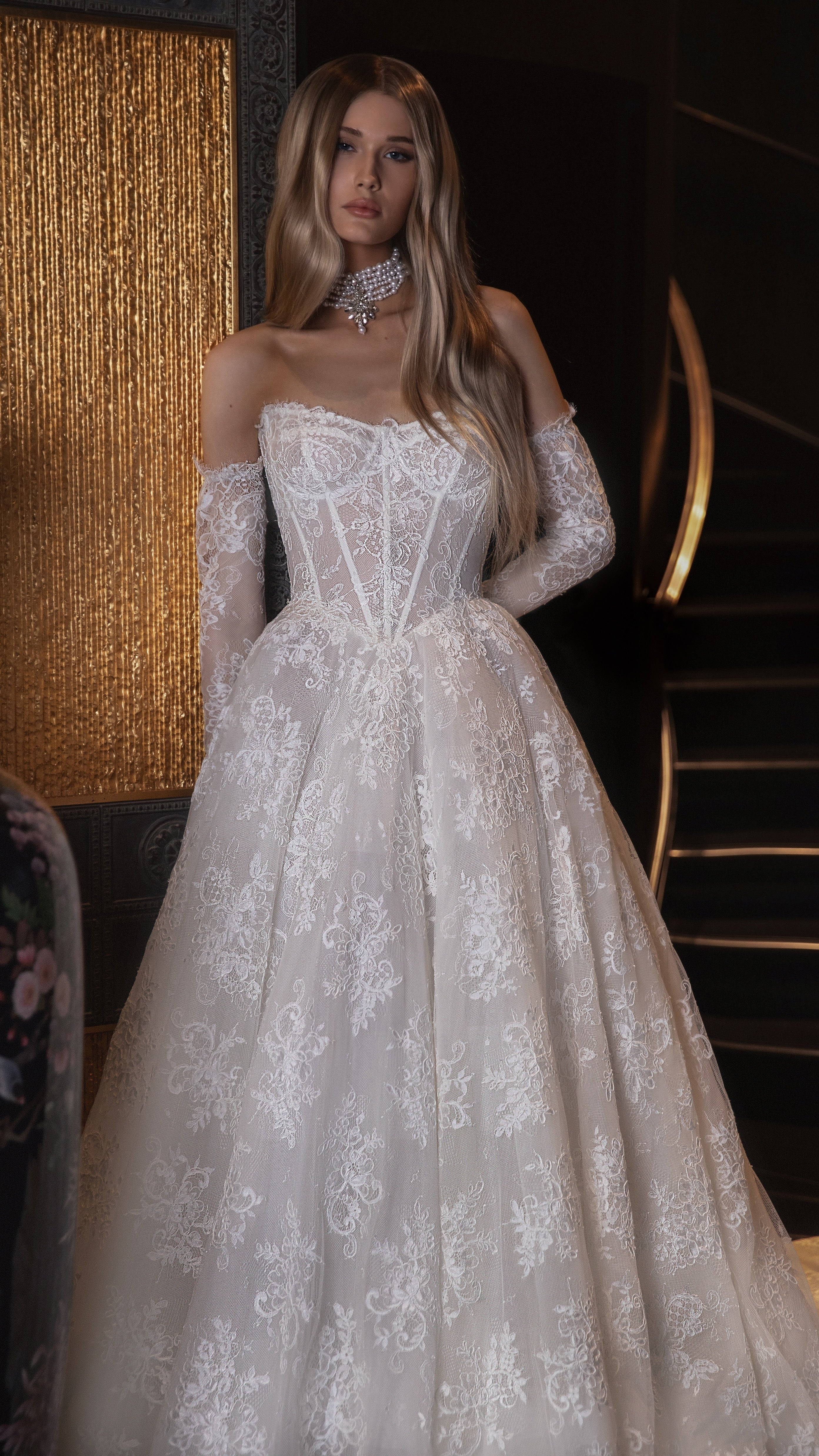 Woman wearing a white lace wedding dress in an elegant indoor setting.