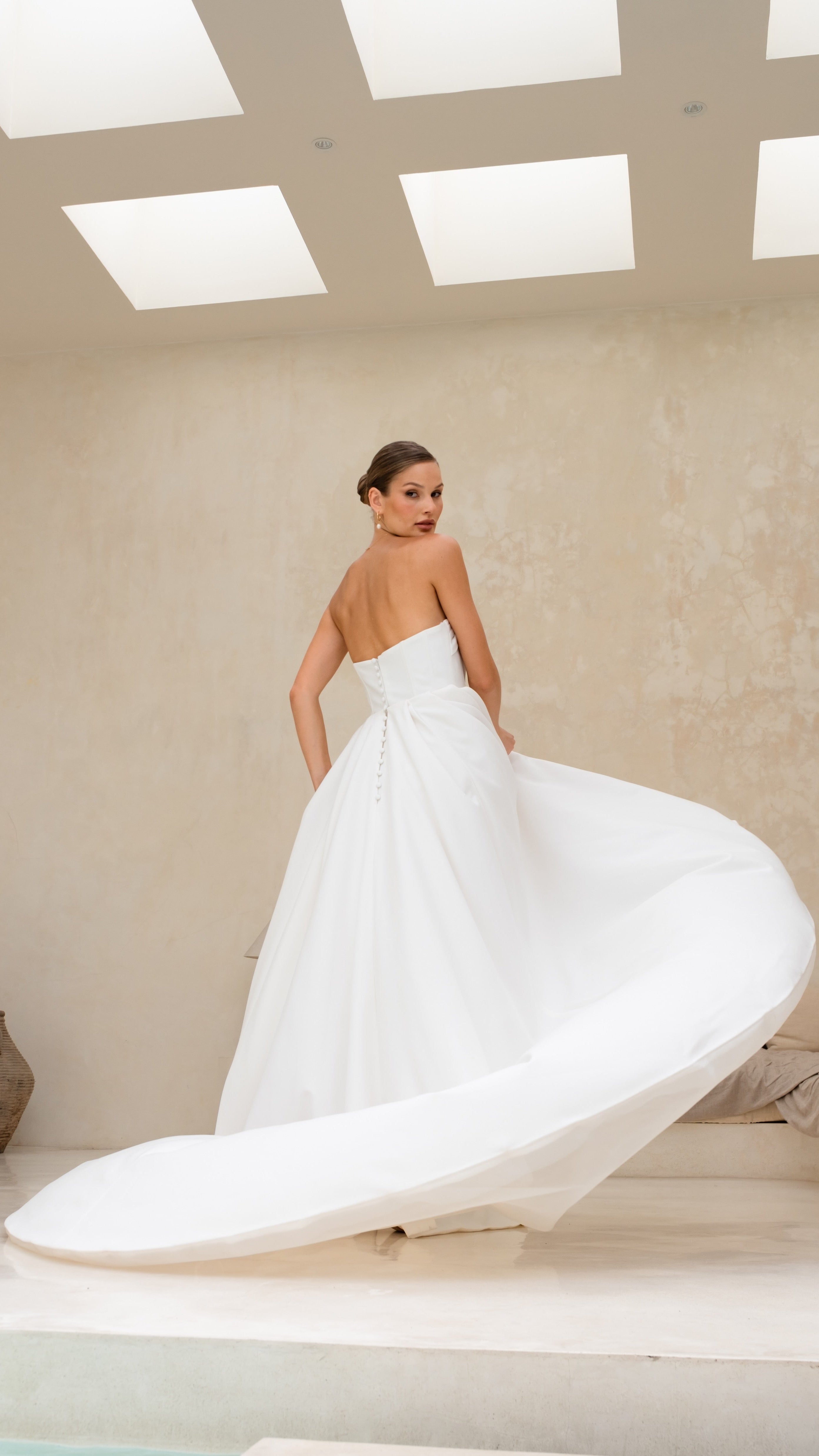 Woman in a white wedding dress with a long train in a minimalistic room.