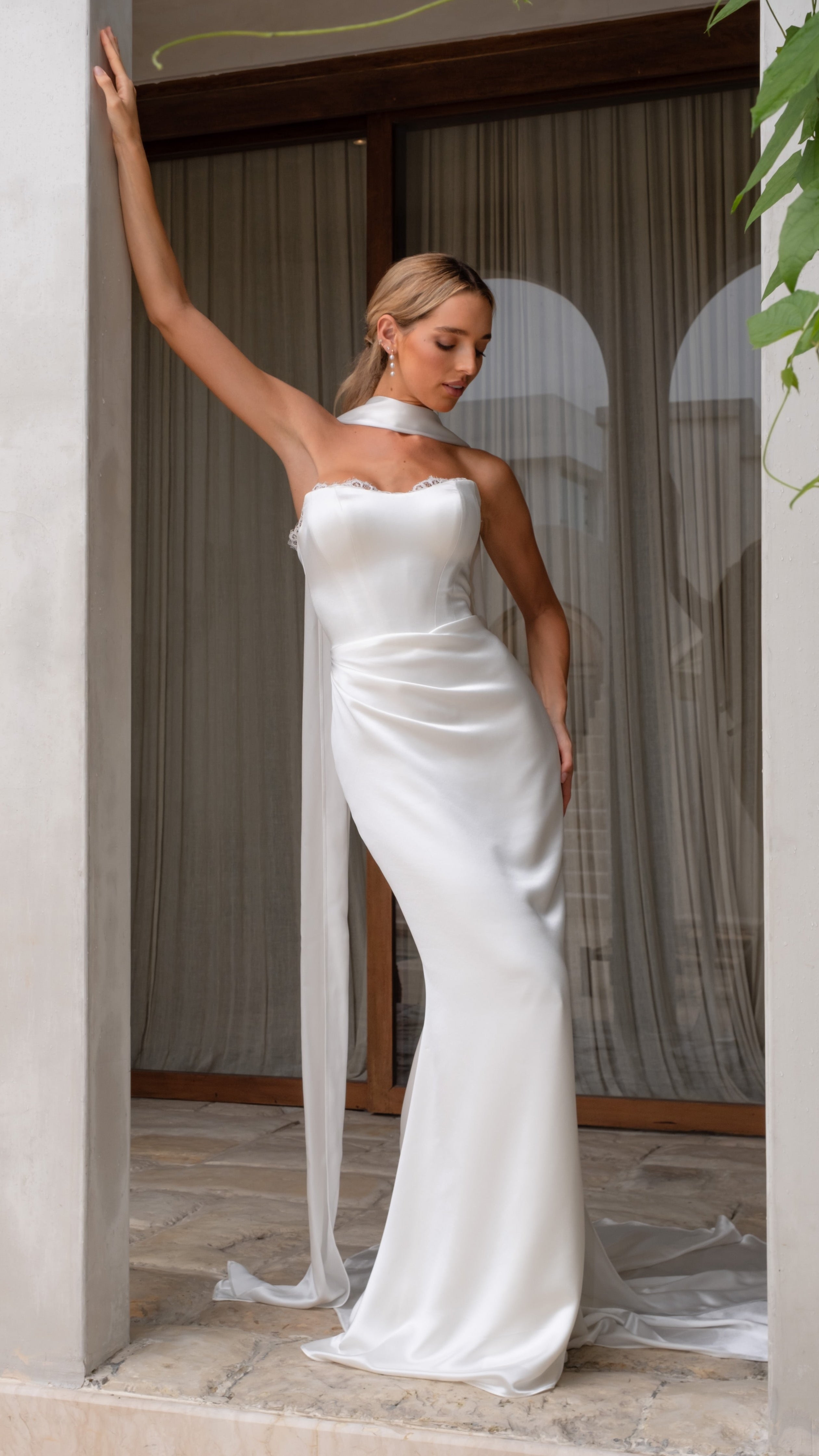 Woman in a white strapless wedding dress standing in a room with columns and curtains.