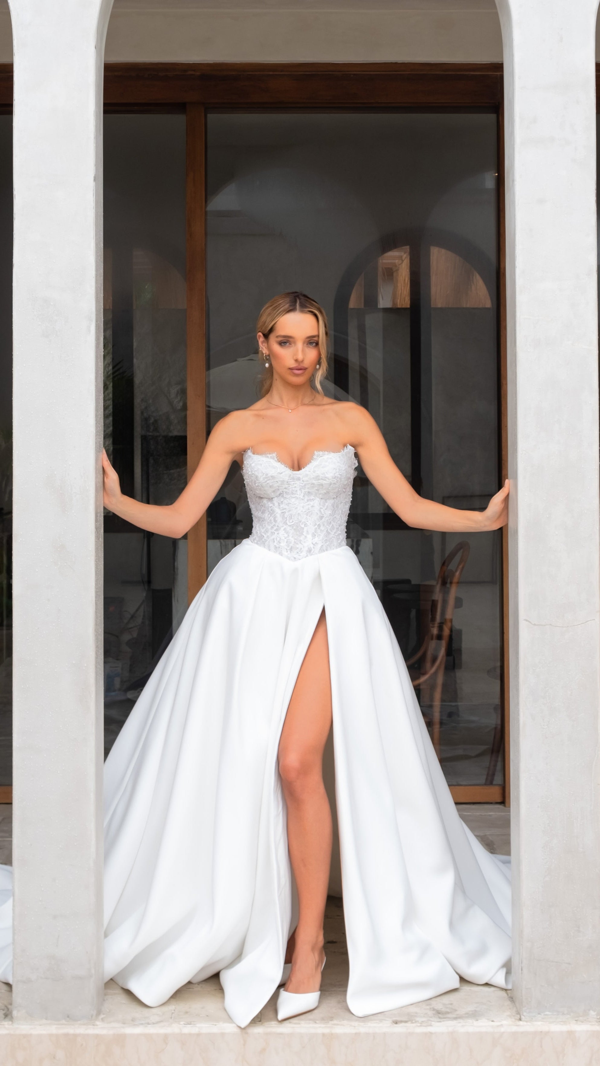 Woman in a white strapless wedding dress with a high slit standing between two columns.