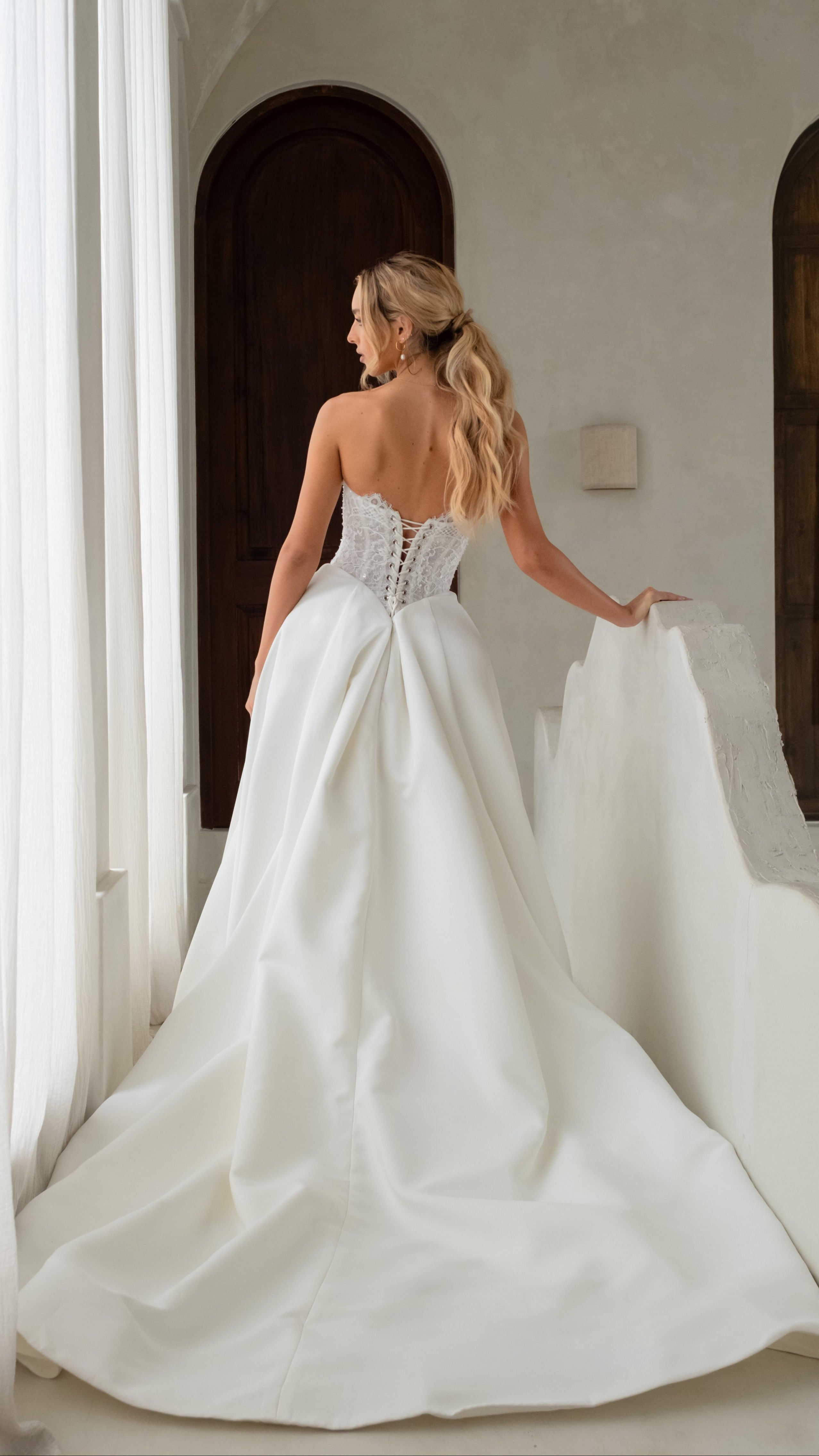 Woman in a white wedding dress standing in a room with arched doorways.