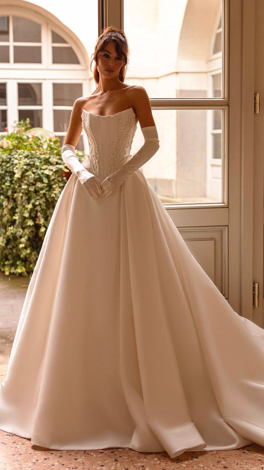 Woman in a white wedding dress standing in a doorway with a garden view.