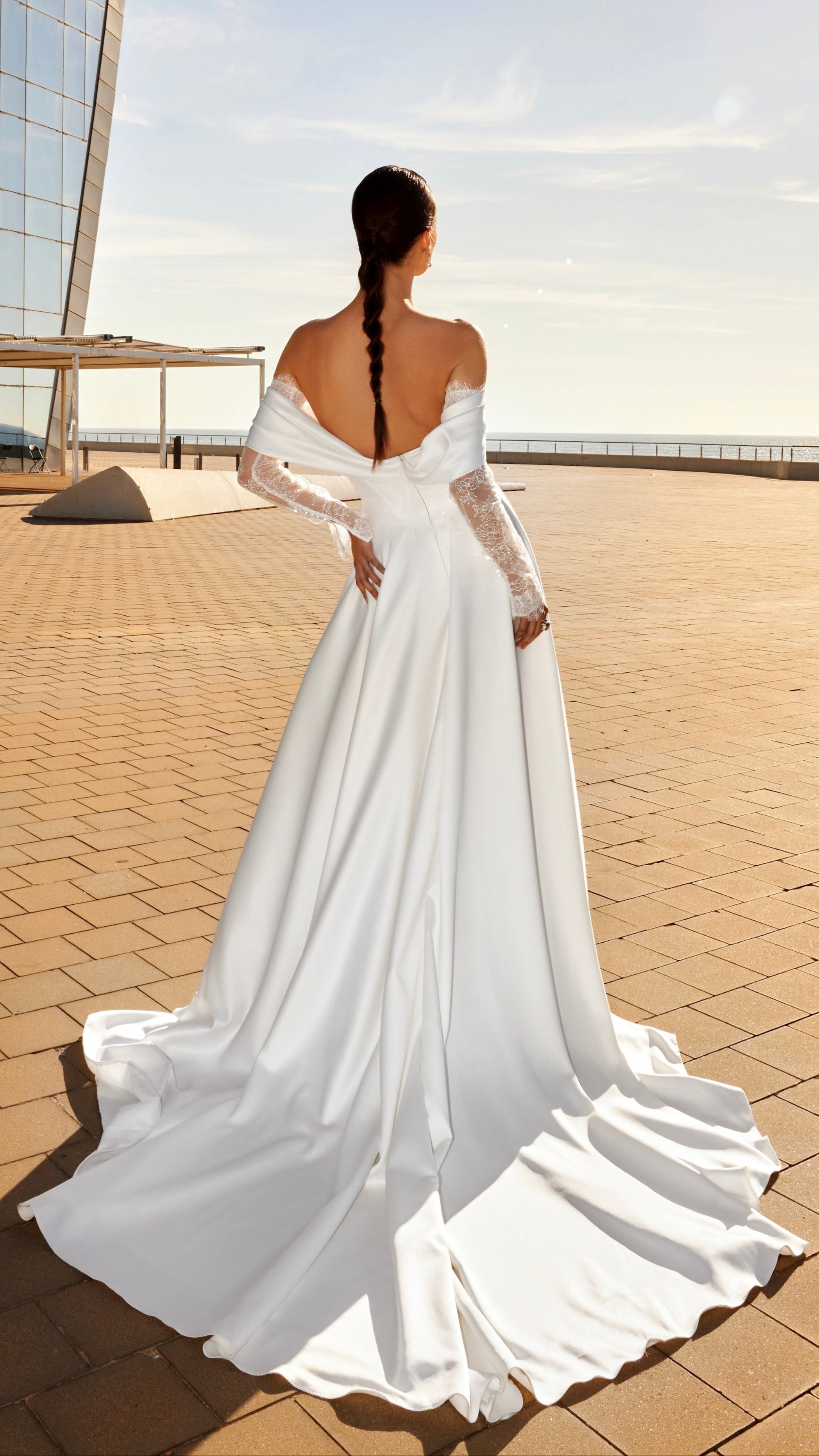 Woman in a white wedding dress standing on a rooftop with modern architecture in the background