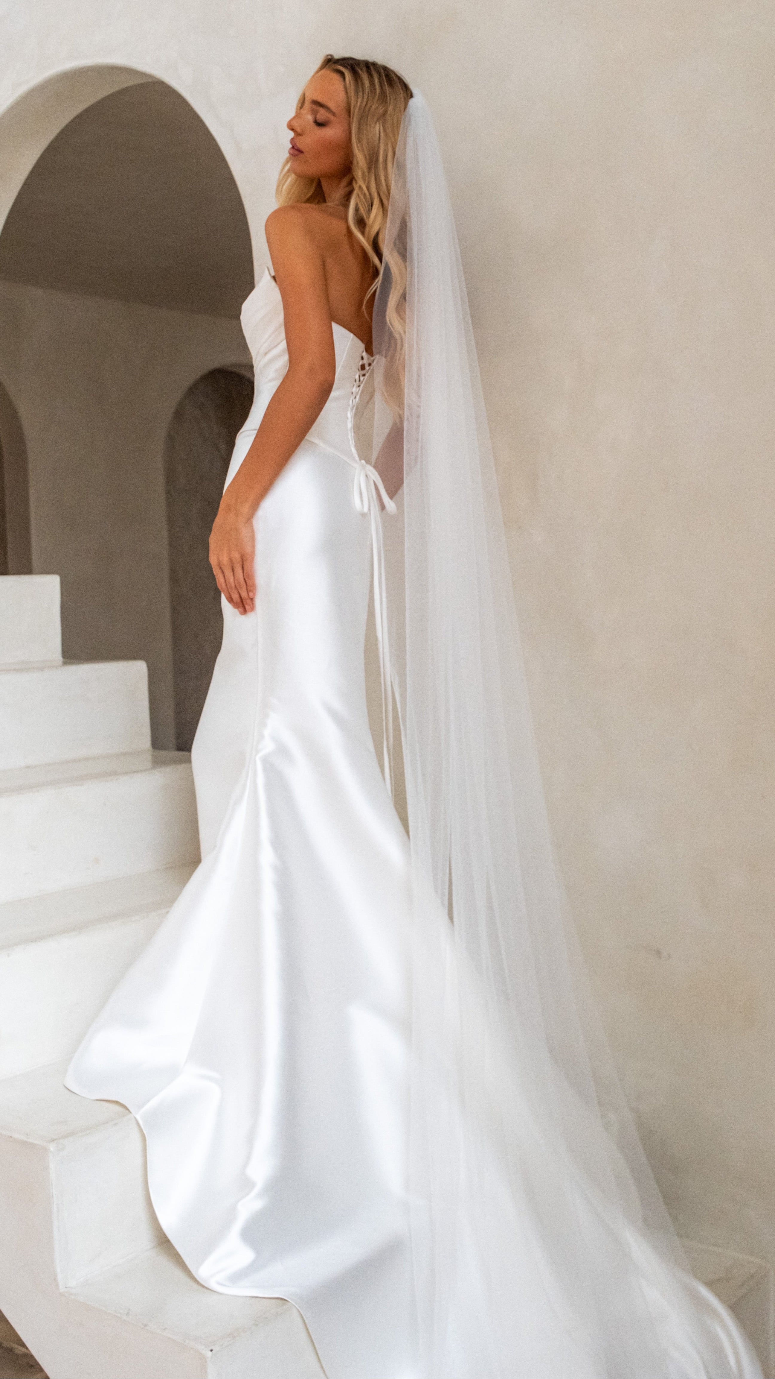 Woman in a white wedding dress with a long veil standing on a staircase.