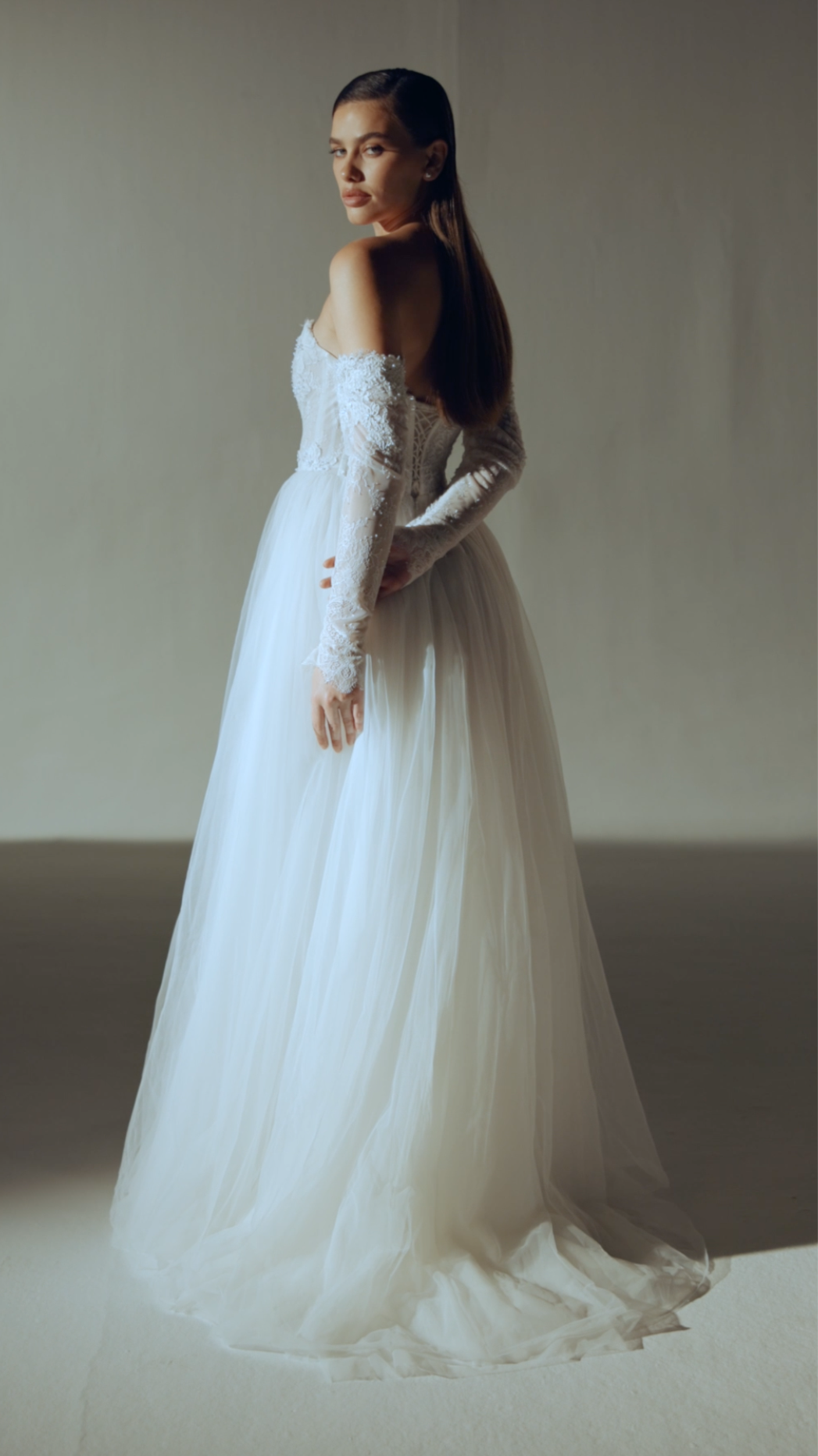 Woman in a white wedding dress standing against a plain background