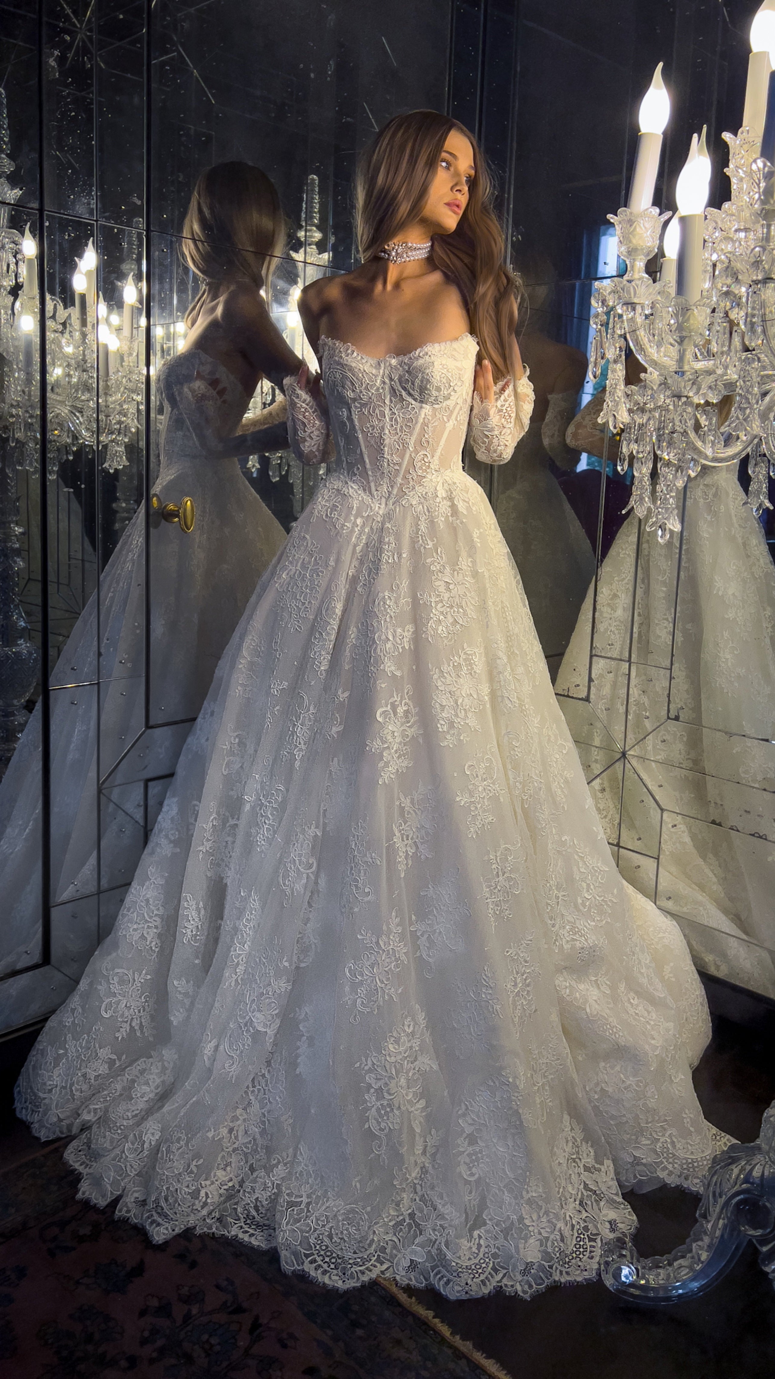Woman in a white lace wedding dress standing in front of a chandelier.