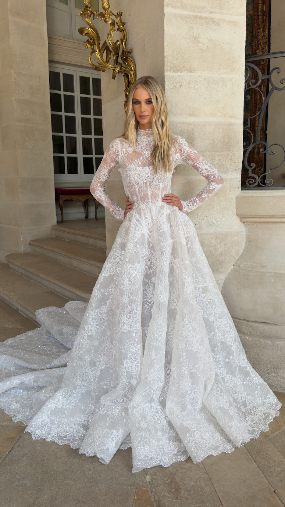 Woman in a white lace wedding dress standing in front of an elegant building.