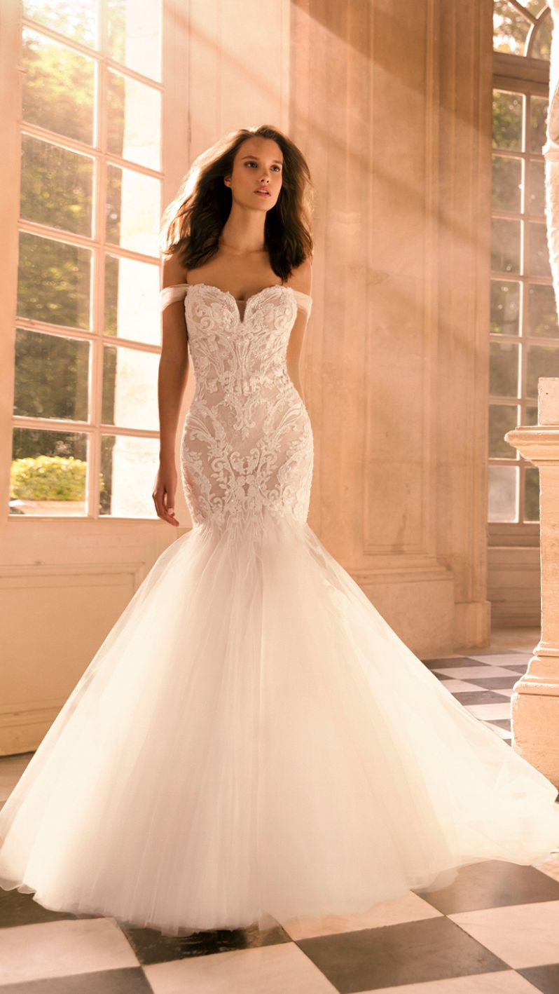 A woman in a ballgown wedding dress with a sweetheart neckline and sleeveless design, standing in a room with a statue and a checkered floor.